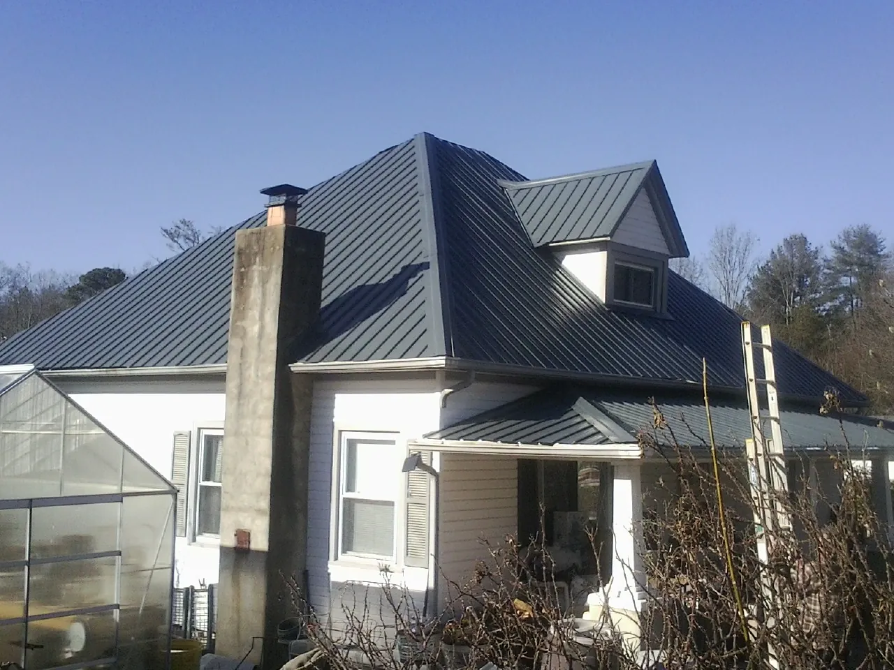 Dark blue standing seam metal roof on a white farmhouse with dormer — Slate & Tile Roof Repair by Roofing Brothers in Aragon