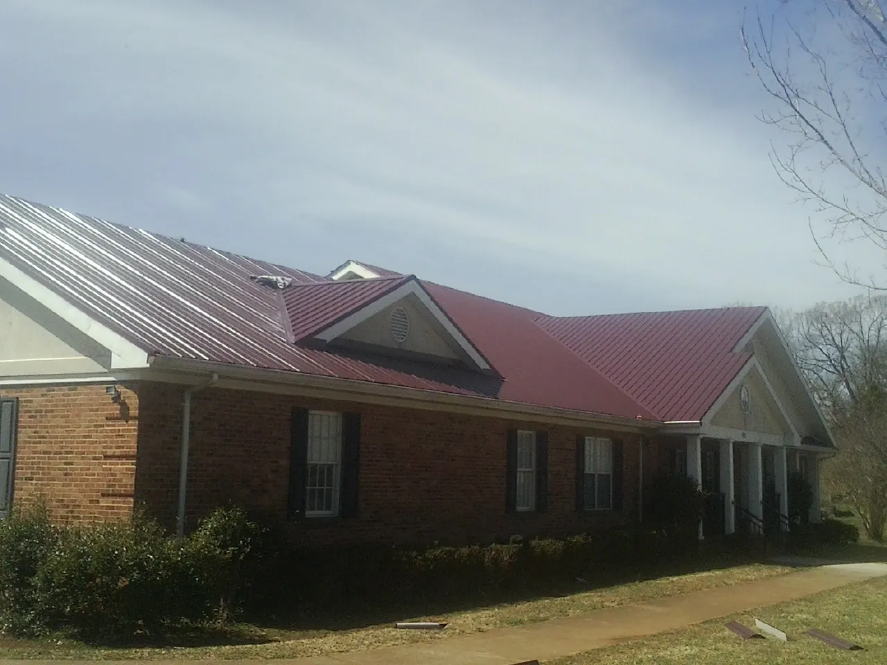 Red metal roof with gabled entries on a long brick building, from a Hail Damage Roof Repair job in Aragon