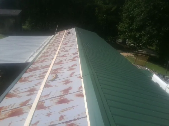 Old rusted panels beside newly installed green metal roofing — Wind Damage Roof Repair by Roofing Brothers in Aragon