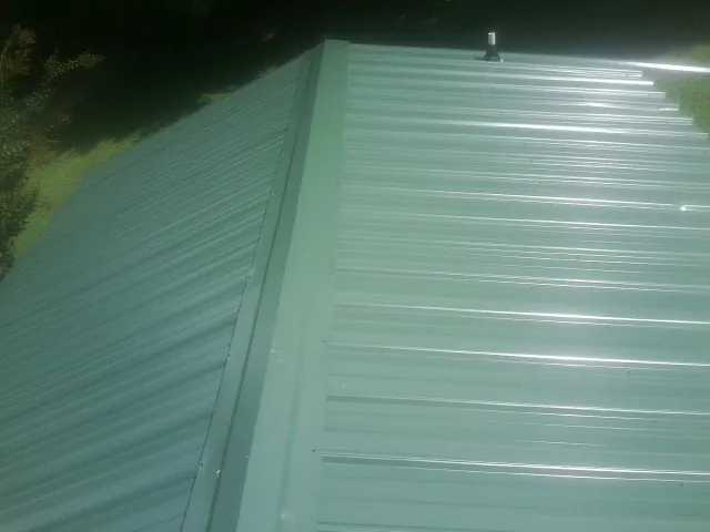 New green metal panels meeting at the ridge of a roof — Flat Roof Repair work by our crew in Aragon