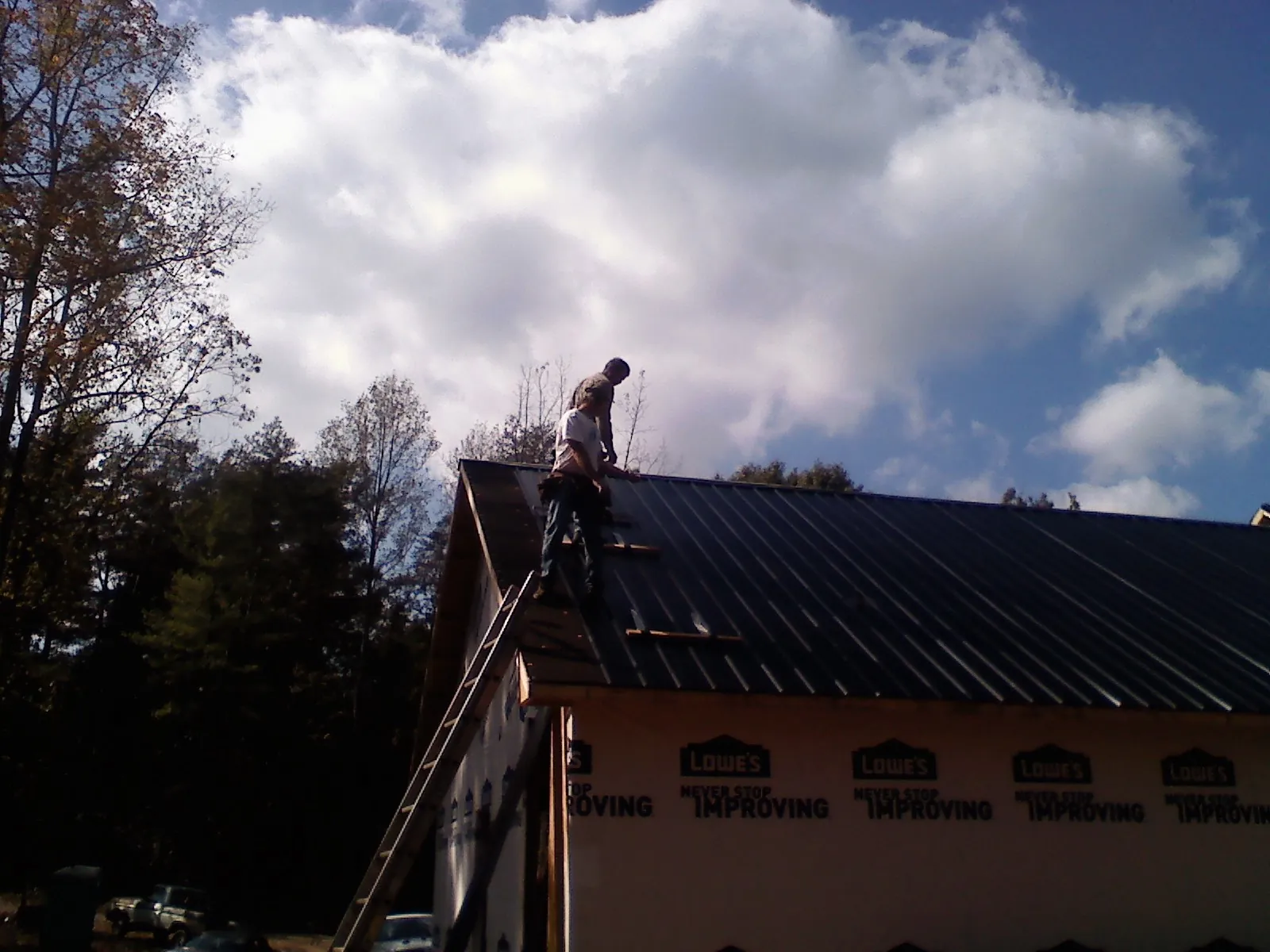 Roofer fastening dark metal panels high against a cloudy sky, from a Roof Inspection job in Aragon
