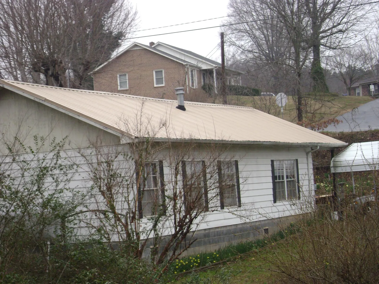 Tan metal roof on a white sided house set into a hillside — Commercial Roofing by Roofing Brothers in Aragon